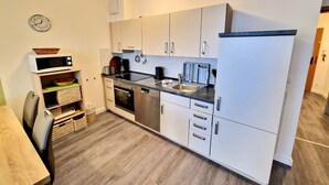 A compact kitchen with white cabinets, a microwave, a sink, and a stove. - Comfortplus vacation apartment with 1 bedroom and terrace on the first floor (Ostseebad Binz)