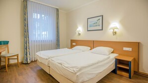 Quarto de hotel com duas camas, uma escrivaninha e uma cadeira.