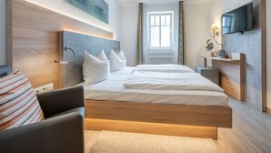 Ett modernt hotellrum med en stor säng, en platt-TV, ett nattduksbord och ett fönster med gardiner.