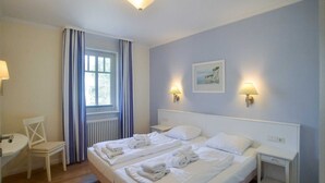 Une chambre d’hôtel avec deux lits, une chaise, un bureau et une fenêtre avec des rideaux.