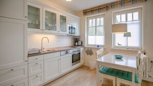 Une cuisine moderne avec des meubles blancs, un four encastré et un coin repas comprenant une table et des chaises blanches.