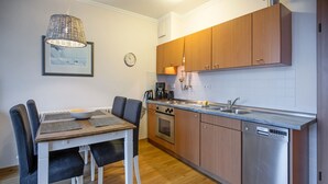 A modern kitchen with wooden cabinets, a stainless steel dishwasher, and a dining table with chairs. - Komfortplus Ferienwohnung mit 1 Schlafzimmer und Balkon im Dachgeschoss (Ostseebad Binz)