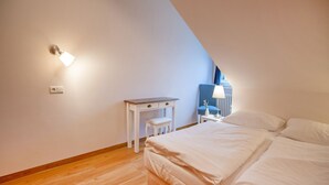 A bedroom with a sloped ceiling, a bed, a nightstand, a lamp, and a chair. - Komfortplus Ferienwohnung mit 1 Schlafzimmer und Balkon im Dachgeschoss (Ostseebad Binz)