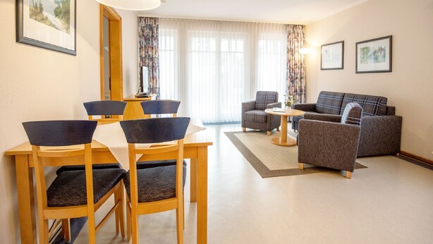A modern living room with a sofa, chairs, a dining table, and a large window with curtains.