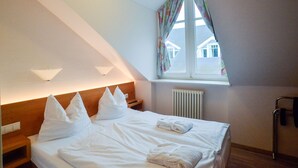 Ett hotellrum med en säng, två sängbord, ett fönster med gardiner, ett element och en sänggavel.