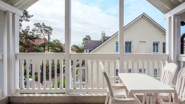 Un patio cubierto con una mesa y sillas blancas, con vistas a una zona residencial con casas y árboles.
