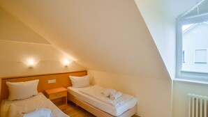 Una habitación pequeña y luminosa, con dos camas, piso de madera y ventana que deja entrar luz natural.