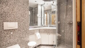 Un baño moderno con encimeras de granito, cabina de ducha de vidrio y lavamanos blanco.