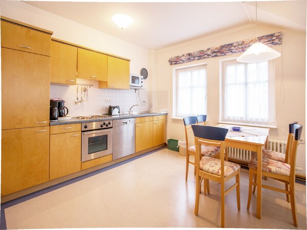 A kitchen with wooden cabinets, a stove, and a dining area with chairs and a table.