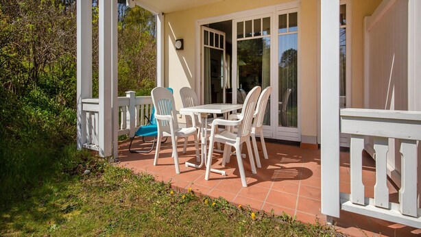 Un patio techado con una mesa y sillas, rodeado por una barandilla blanca y un vidrio que da al interior.