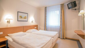 Habitación de hotel con dos camas, un escritorio, televisor montado en la pared y una ventana con cortinas.
