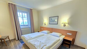 A hotel room with a large bed, two bedside tables, a chair, a window with curtains, and a framed picture on the wall.