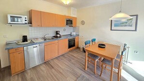 A compact kitchen with wooden cabinets, a microwave, a coffee maker, and a dining area with a table and chairs.