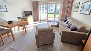A modern living room with a sofa, chairs, a dining table, and a TV.
