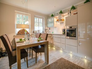 A modern kitchen with white cabinets, a Bosch oven, and a dining area with a wooden table and chairs. - Comfort plus apartment with 1 bedroom and balcony on the upper floor (Ostseebad Binz)