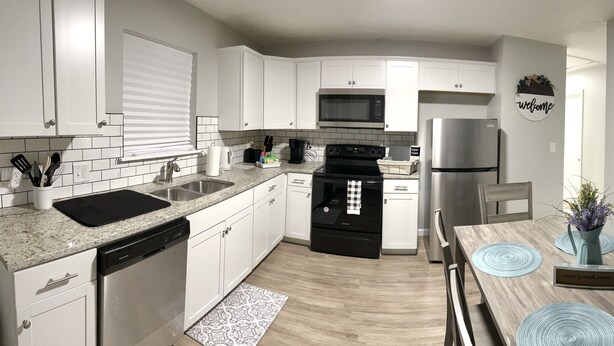 A modern kitchen with white cabinets, a stainless steel refrigerator, and a dining area with a wooden table and blue placemats.