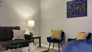 A living room with a dark blue sofa, a coffee table with decorative items, a lamp, and a wall-mounted abstract art piece.
