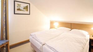 Una camera d'albergo con un letto rifatto, un comodino con una lampada, un quadro appeso alla parete e una sedia.