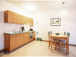 A compact kitchen with wooden cabinets, a sink, a stove, and a dining area with a table and chairs.