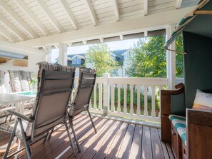 Une terrasse couverte avec deux chaises et une table, une terrasse en bois et une clôture blanche donnant sur un quartier résidentiel.
