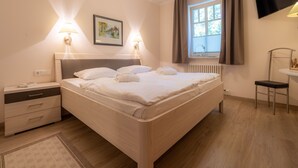 Ein ordentlich eingerichtetes Schlafzimmer mit einem großen Bett, Nachttischlampen, einem kleinen Tisch, einem Sessel und einem an der Wand befestigten Fernseher.