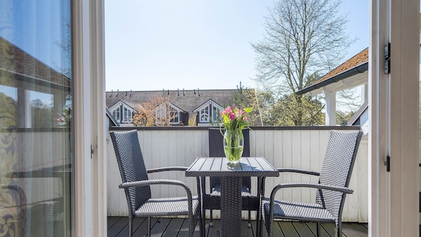 En uteplats med ett bord och två stolar, en vas med blommor och utsikt över de omkringliggande husen.
