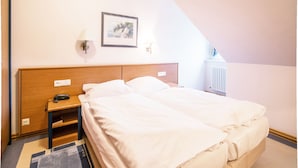 Ett hotellrum med en säng, ett nattduksbord, en lampa, en inramad tavla på väggen och ett element.