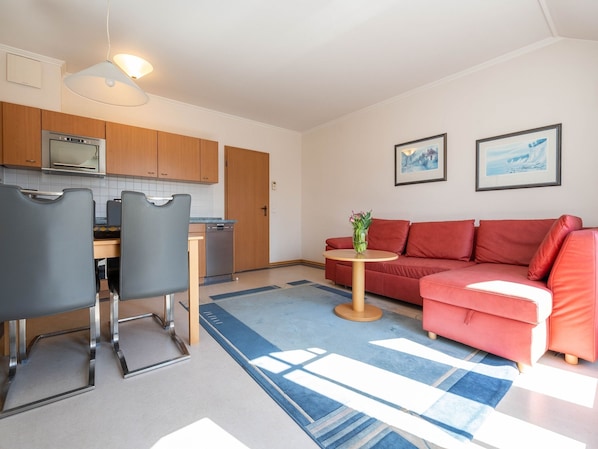 Un espace de vie compact comprenant un coin cuisine, un canapé rouge, une petite table ronde avec un vase et deux tableaux encadrés accrochés au mur.