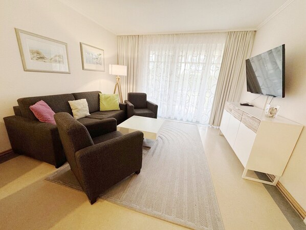 Ein Hotelzimmer mit einer Sitzecke, einem kleinen Tisch, einem Sessel, einem Fernseher und einer Lampe.