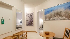 A hotel room with a bed, a wooden bench, a round table with a bowl, and a painting of a beach scene. - Comfort apartment with 2 bedrooms and terrace on the first floor (Ostseebad Binz)