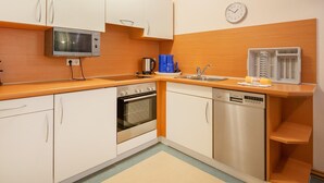 A compact kitchen with white cabinets, a microwave, an oven, a dishwasher, and a coffee maker. - Comfort apartment with 2 bedrooms and terrace on the first floor (Ostseebad Binz)