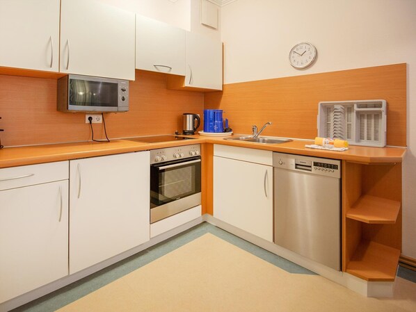 Una cocina compacta con gabinetes blancos, microondas, horno, lavavajillas y cafetera.