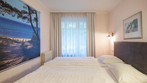 A hotel room with a large bed, a view of the sea through sheer curtains, a painting on the wall, and a nightlight. - Comfort apartment with 2 bedrooms and terrace on the first floor (Ostseebad Binz)