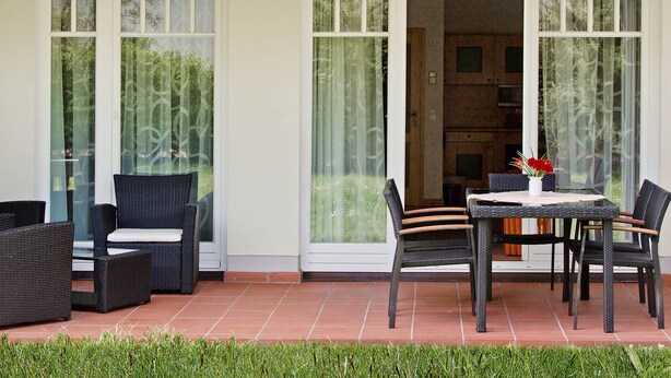 A patio area with wicker furniture, a table with chairs, and a vase with flowers. - Comfort apartment with 2 bedrooms and terrace on the first floor (Ostseebad Binz)