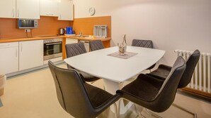 A compact kitchen with a dining area, featuring a white table, four chairs, a clock, and basic appliances. - Comfort apartment with 2 bedrooms and terrace on the first floor (Ostseebad Binz)
