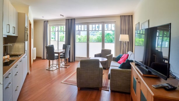 A modern living room with a dining area, a sofa, a TV, and a kitchen with cabinets and a stove. - Comfort apartment with 1 bedroom and terrace on the first floor (Ostseebad Binz)