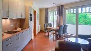A modern kitchen with a dining area, large windows, and a view of greenery. - Comfort apartment with 1 bedroom and terrace on the first floor (Ostseebad Binz)