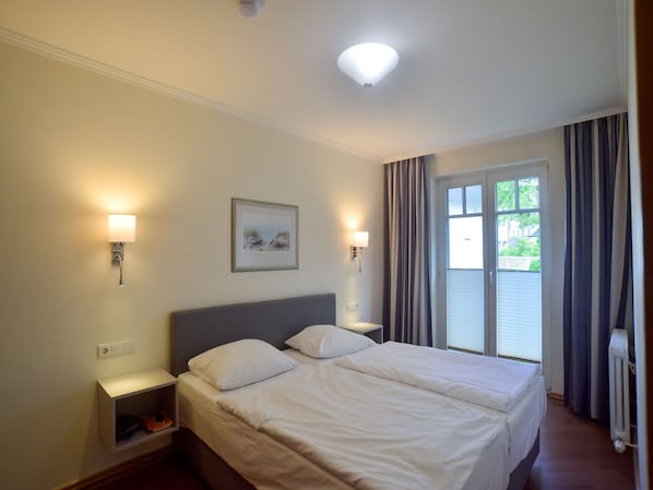 Une chambre d’hôtel comprenant un lit, deux tables de chevet, une commode, une fenêtre avec des rideaux et un luminaire au plafond.