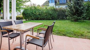 An outdoor patio with a table and chairs, surrounded by a well-maintained lawn and trees. - Comfort apartment with 1 bedroom and terrace on the first floor (Ostseebad Binz)