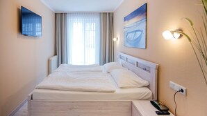 A neatly arranged hotel room with a large bed, a bedside table with a remote control, and a wall-mounted TV. - Comfortplus vacation apartment with 1 bedroom and terrace on the first floor (Ostseebad Binz)