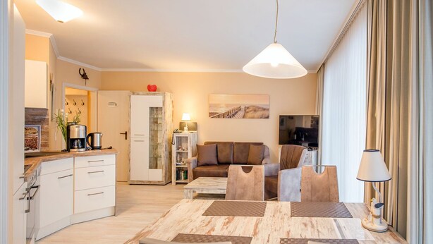 A modern kitchen with white cabinets, a coffee machine, and a dining table with chairs. - Comfortplus vacation apartment with 1 bedroom and terrace on the first floor (Ostseebad Binz)