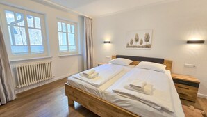 Una cama doble con sábanas y toallas blancas, un cabecero de madera, una mesita de noche y una lámpara de pared.