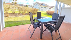 Un patio al aire libre con una mesa y sillas, piso de baldosas y vista a casas y árboles al fondo.
