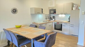 Una cocina moderna con comedor, que incluye una mesa de madera, sillas azules, un tazón amarillo y varios electrodomésticos.