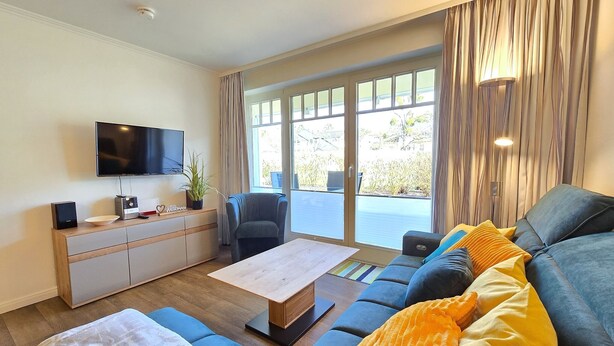 Una sala de estar moderna con un sofá, una mesa de centro, un televisor y un ventanal corredero que da a un espacio exterior.