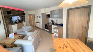 Ein modernes Wohnzimmer mit einer Couch, einem Holzesstzimmer und einer Küchenzeile inklusive Mikrowelle und Spüle.