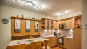 Een moderne keuken met houten kastjes, een centraal eiland met barkrukken, een klok aan de muur en een decoratief kunstwerk met wijnmotieven.