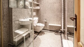 Een moderne badkamer met een wastafel op een granieten blad, een toilet, een douchehoek en een glazen wastafelmeubel.