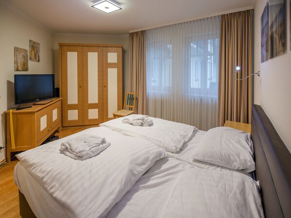 A hotel room with two beds, a TV, a wardrobe, and a window with curtains. - Comfort Plus Apartment with 2 bedrooms and a balcony on the top floor (Ostseebad Binz)