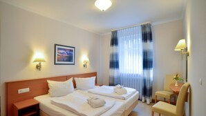 A hotel room with a double bed, two bedside tables, a chair, a small table, and a window with curtains.